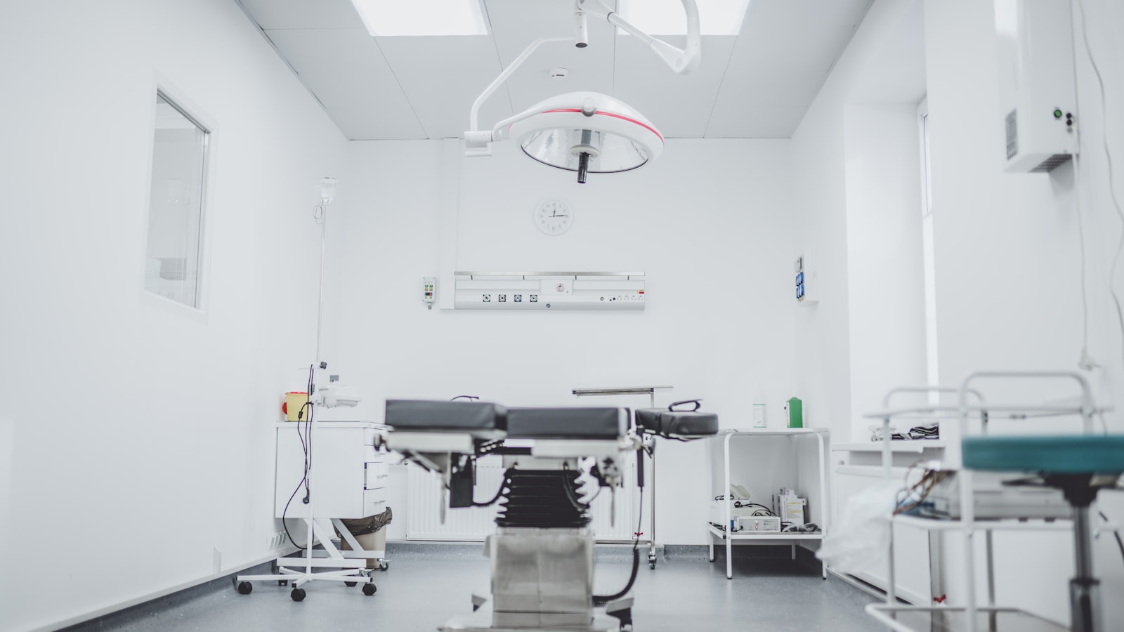 Bright treatment room with an examination table, procedure lamp, and a wall-mounted medical services panel